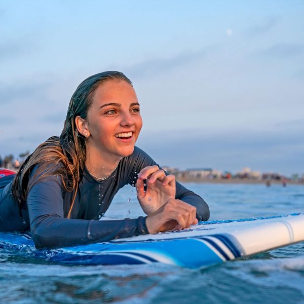 woman smiling while floating on the ocean using her surfboard