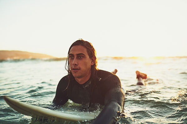 Shot of a young man paddling on a surfboard and riding the surf tide