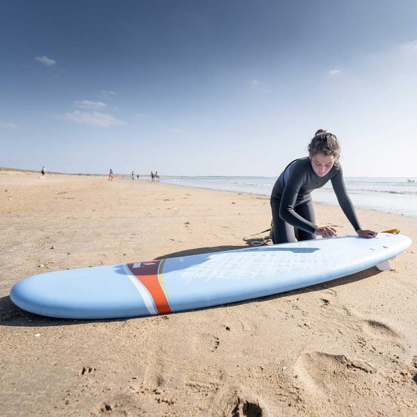 woman waxing a surfboard on a beach